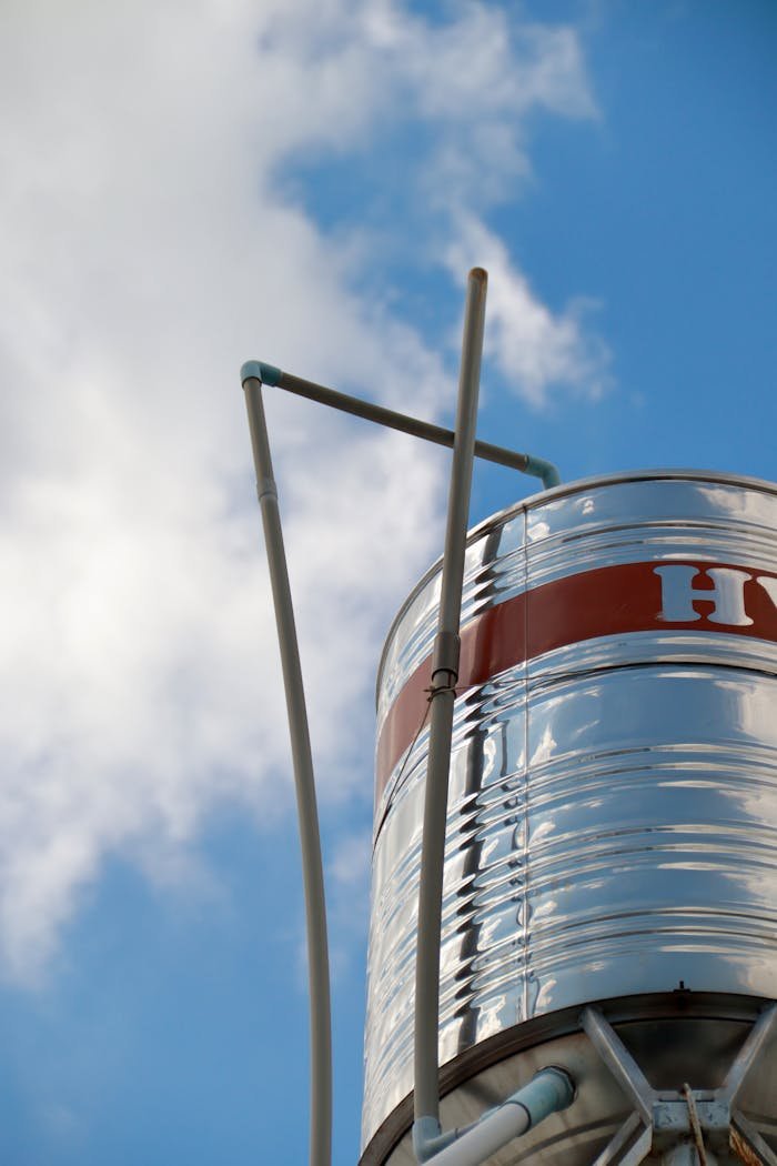 A shiny metal water tank standing tall under a bright blue sky with clouds.