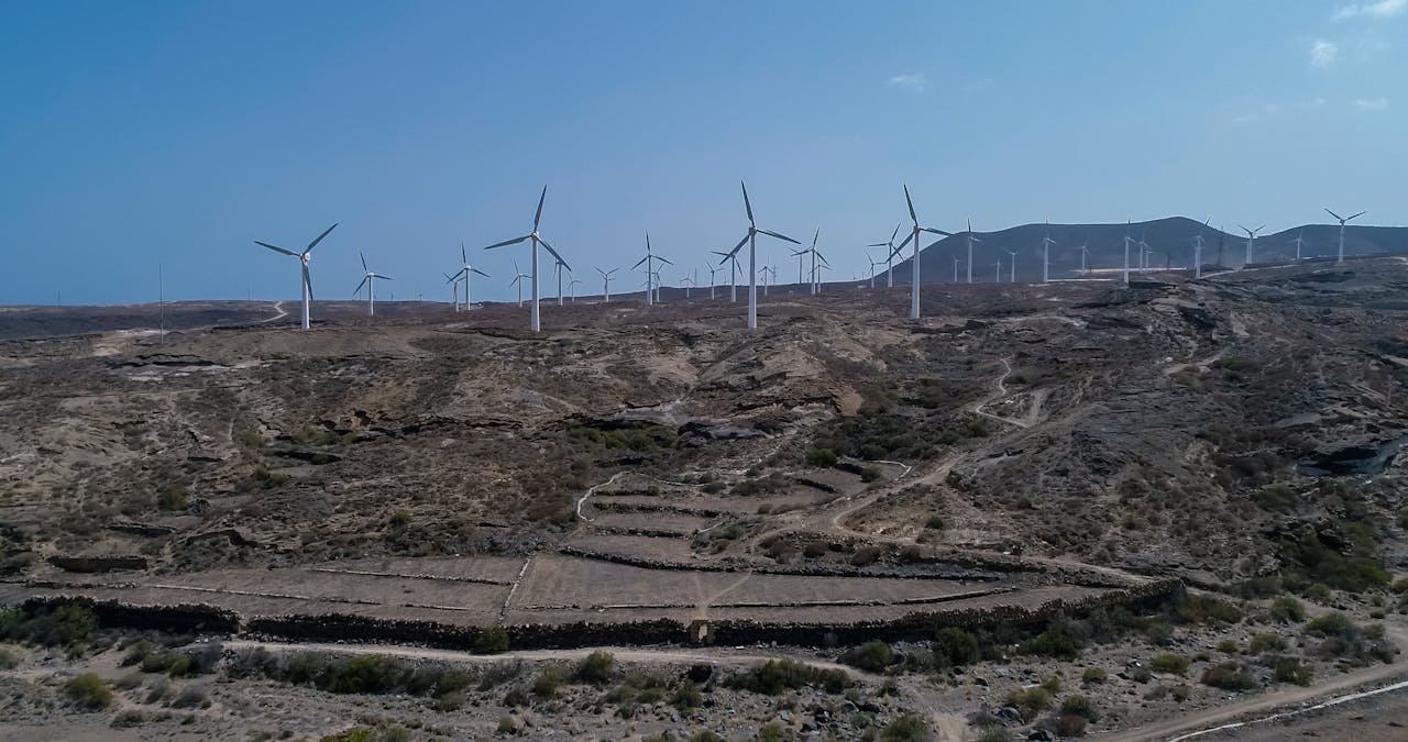 services-02 Aerial image capturing a vast wind farm set in a barren desert landscape under clear skies.