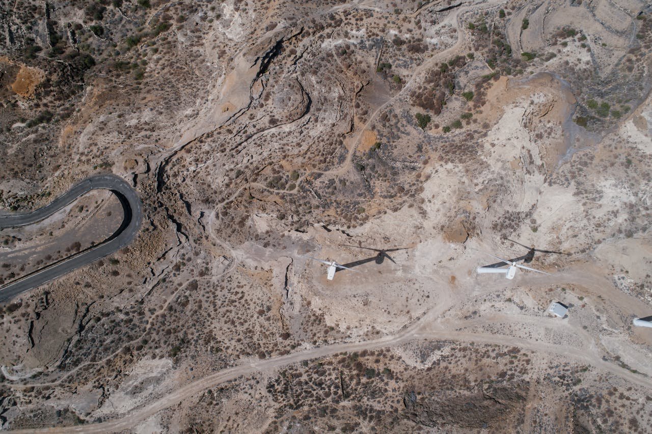 services-04 Drone shot of wind turbines in a dry, arid terrain with winding roads.